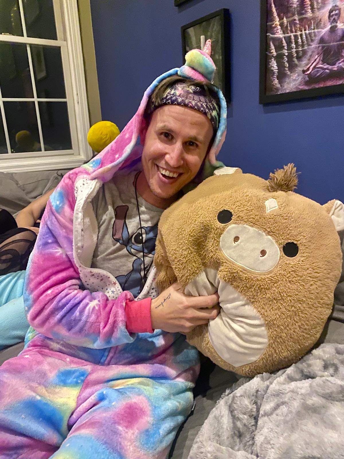 Kai grinning in a rainbow unicorn onesie, hugging a big plush toy