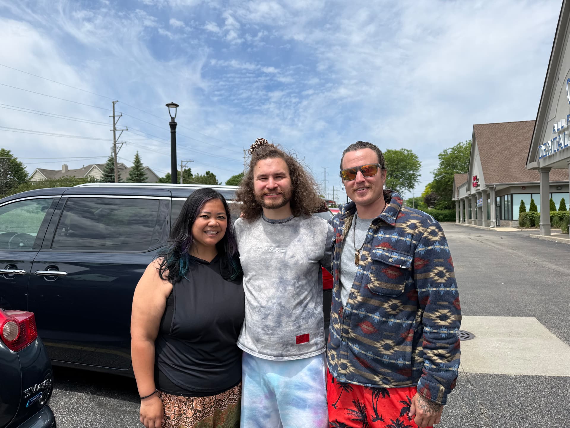 Joanna, David and Kai smiling together in a sunny parking lot