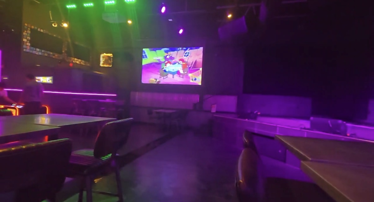 The dance floor at Life Bar Arcade, lit in purple and green with a large screen