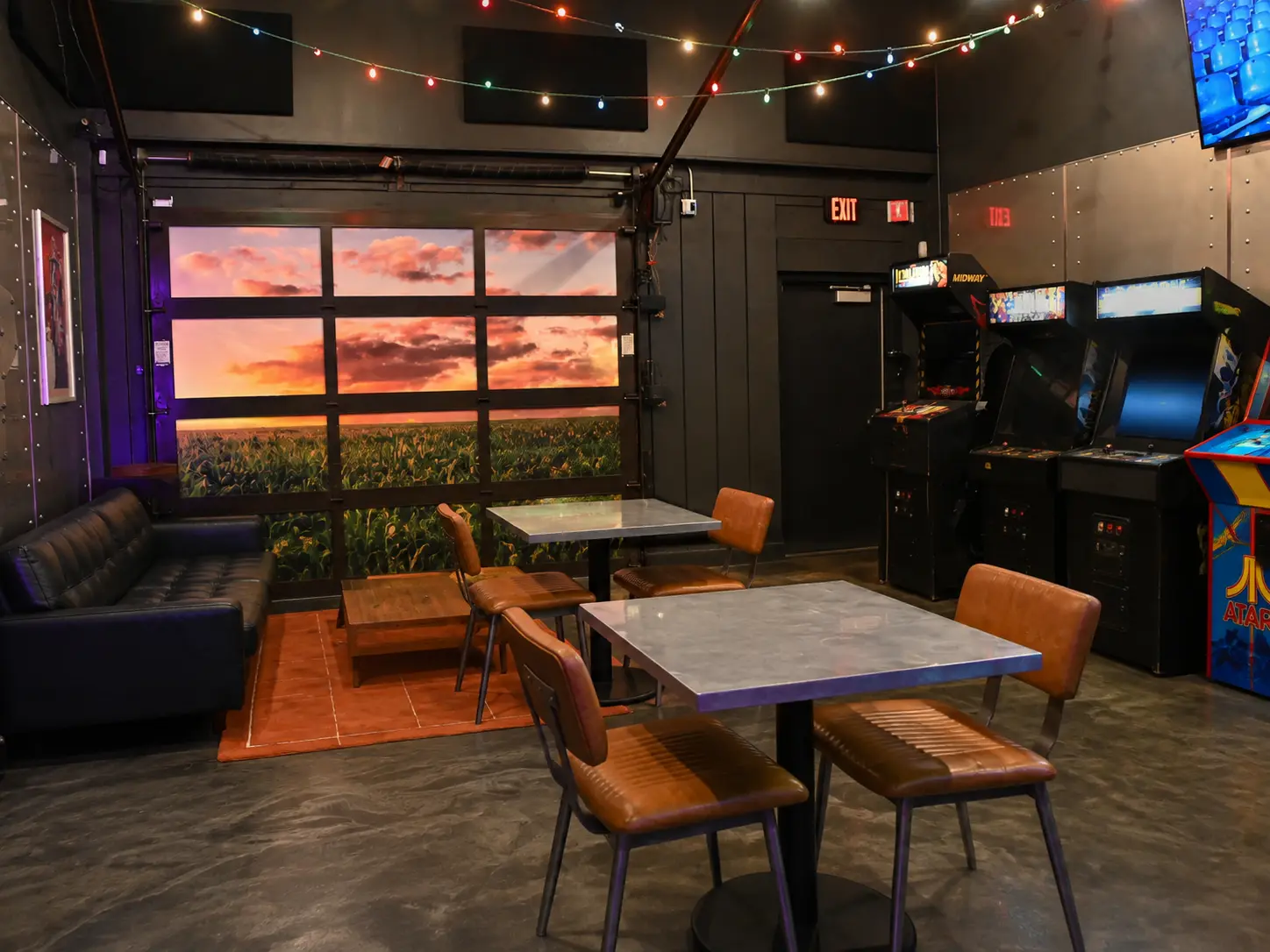 The quiet back room at Life Bar Arcade with string lights, seating and arcade cabinets