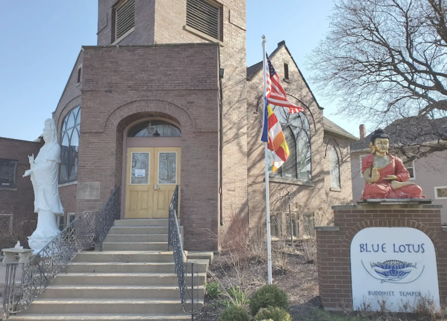 The brick entrance of Blue Lotus Buddhist Temple in Woodstock with a red Buddha statue beside the sign