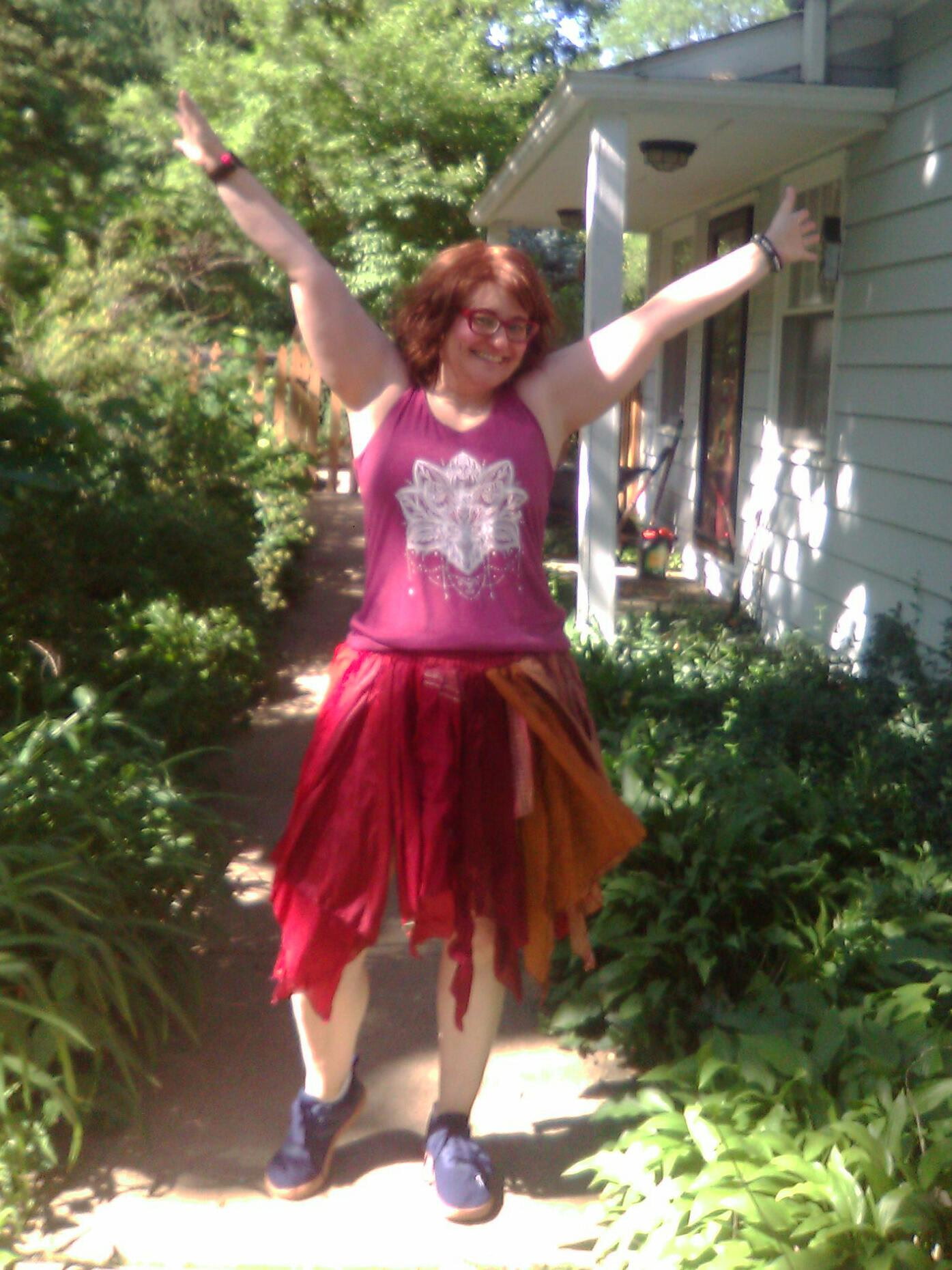 Vilija with arms raised joyfully on a sunny garden path