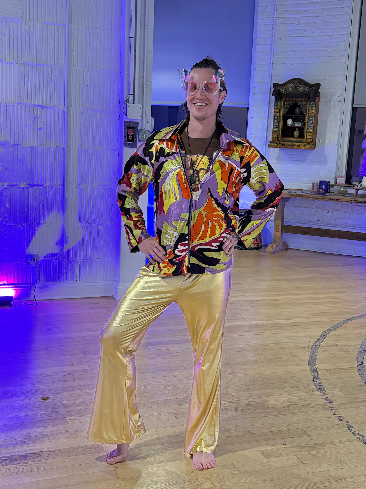 Kai posing in heart-shaped unicorn glasses, a bold patterned jacket and gold flared pants